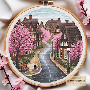 May include: Cross stitch pattern depicting a charming street scene with colourful houses and blooming pink cherry blossom trees. The street is lined with lampposts and a winding path leads to the centre of the image.