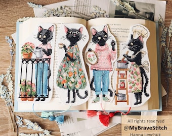 May include: Four cross-stitch bookmarks featuring black cats in various activities: gardening on a balcony, holding a book, embroidery, and cooking in a chef hat. Each bookmark has a colorful tassel at the bottom and is displayed on an open book.
