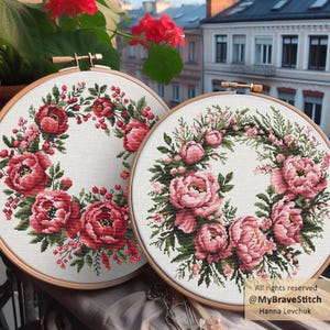 Puede incluir: Dos coronas florales de punto de cruz en aros de madera. Una corona presenta peonías y bayas de color rojo intenso, la otra tiene peonías rosas. Ambas están sobre un fondo blanco, con follaje verde. El fondo muestra un paisaje urbano.