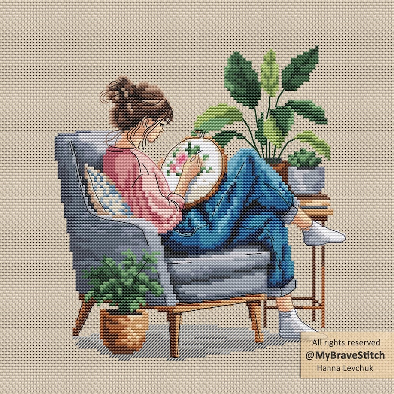 May include: Cross-stitch art of a person seated in a gray armchair, cross-stitching a floral design. The person wears a pink shirt and blue jeans. Potted plants and a small side table are nearby. The artwork is set against a neutral background.