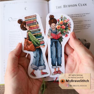 Peut inclure: Deux marque-pages en point de croix. L'un représente une personne portant des livres, l'autre lisant avec des fleurs. Les deux personnages portent des salopettes en jean et des chaussures rouges. Les marque-pages sont devant un livre ouvert. Le tag indique "MyBraveStitch".