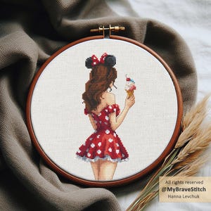 Op de afbeelding: Kruissteekborduurwerk in een houten hoepel met een cartoonvrouw in een rode polkadotjurk en zwarte muizenoren, die een ijsje vasthoudt. Het borduurwerk staat op witte stof. De tekst luidt "All rights reserved @MyBraveStitch Hanna Levchuk."