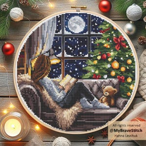 Puede incluir: Bordado de punto de cruz en un aro de madera que representa una escena invernal. Una persona lee junto a una ventana con vista a una noche estrellada y un &aacute;rbol de Navidad. Un osito de peluche est&aacute; cerca. El texto "All rights reserved @MyBraveStitch Hanna Levchuk" es visible.