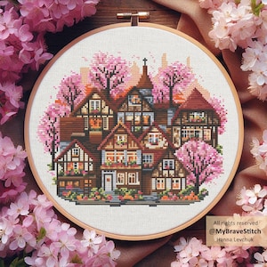 May include: Cross-stitch embroidery of a village scene with brown houses, pink cherry blossom trees, and a wooden frame. The text "All rights reserved @MyBraveStitch Hanna Levchuk" is in the lower right corner.