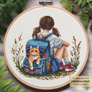 Könnte beinhalten: Ein runder Holzstickrahmen mit einem Kreuzstichmuster, das eine Person mit braunen Zöpfen zeigt, die mit einem blauen Rucksack sitzt. Eine orangefarbene getigerte Katze schaut aus dem Rucksack hervor. Das Design enthält hohes Gras und Blumen.