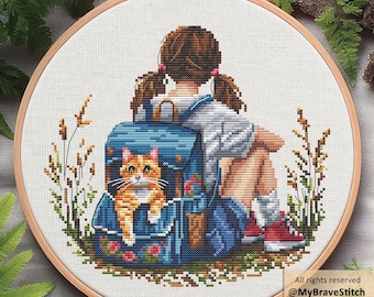 May include: A circular wooden embroidery hoop containing a cross-stitch pattern of a person with brown pigtails sitting with a blue backpack. An orange tabby cat peeks out from the backpack. The design includes tall grasses and flowers.