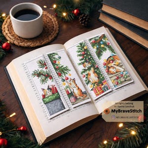 Op de afbeelding: Vier kruissteek bladwijzers met kerstthema's, met katten, kerstbomen en cadeaus. De bladwijzers liggen in een open boek, met een kopje koffie en feestelijke decoraties op de achtergrond. De bladwijzers zijn ongeveer 5 x 15 cm groot.