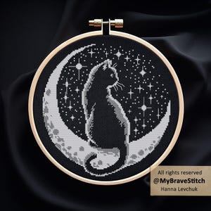 May include: Cross-stitch art of a black cat sitting on a crescent moon, surrounded by stars, set against a black background. The design is framed in a wooden embroidery hoop. Text on the bottom right corner reads "All rights reserved @MyBraveStitch Hanna Levchuk."