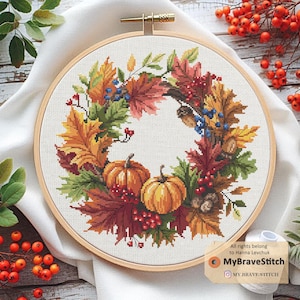 Könnte beinhalten: Kreuzstich-Stickerei in einem Holzreifen mit einem Herbstkranz-Design. Der Kranz enthält bunte Herbstblätter, Kürbisse, Beeren und Eicheln. Der Text "MyBraveStitch" ist unten rechts sichtbar.