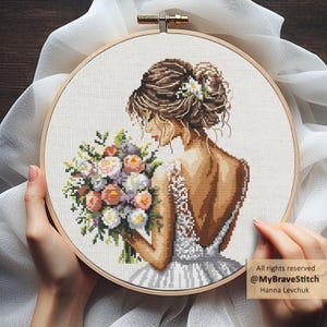 May include: A cross-stitch embroidery in a circular wooden hoop depicting a person with brown hair in an updo, wearing a white dress, and holding a colorful floral bouquet. The text "All rights reserved @MyBraveStitch Hanna Levchuk" is visible.