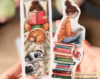 May include: Two rectangular fabric bookmarks featuring cross-stitch embroidery. One shows a person reading in bed with a cat and dog. The other shows a person sitting on a stack of books reading. Text on the image reads: All rights reserved @MyBraveStitch Hanna Levchuk.