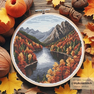 May include: A cross-stitch landscape in a wooden hoop, showing a river scene with autumn colours. The trees are in shades of orange, red, and yellow, with a light blue sky. The text "All rights reserved @MyBraveStitch Hanna Levchuk" is visible. Craft supplies are in the background.