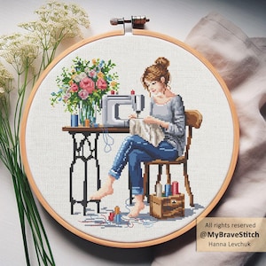 Op de afbeelding: Kruissteek borduurring met een vrouw die naait aan een tafel met een naaimachine. Een vaas met bloemen staat op de tafel. Spoelen garen en een houten kistje staan in de buurt. De tekst "All rights reserved @MyBraveStitch Hanna Levchuk" staat rechtsonder.
