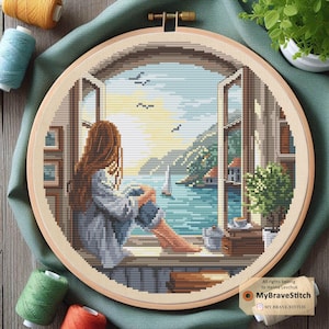 Op de afbeelding: Een kruissteek borduurring met een schilderachtig uitzicht door een raam. Het kunstwerk toont een persoon die uitkijkt op een baai met bergen, een zeilboot en vogels. Het kleurenpalet omvat blauw, groen en bruin. De tekst "MyBraveStitch" is zichtbaar.