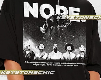 May include: Black t-shirt with a white graphic print of a horse bucking and the word "NODE" in large white letters. The text "This dream you're chasing, where you end up at the top of the mountain, all eyes on you... it's the dream you never wake up from." is printed below the graphic. The text "KEYSTONECHIC" is printed at the bottom of the shirt.