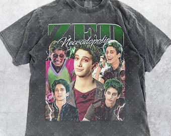 Puede incluir: Camiseta gris oscuro con un collage de imágenes y el texto "ZMD Necropolis". Las imágenes muestran personajes con pelo verde y maquillaje. La camiseta tiene un aspecto vintage y desgastado.