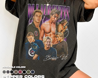 Puede incluir: Camiseta negra con un diseño que presenta varias imágenes de un hombre, el texto "DI LAURENTIIS" en morado y blanco, y el texto cursivo "Brian U". Los colores disponibles se enumeran debajo del diseño.