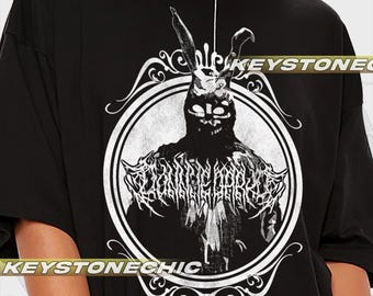 Puede incluir: Camiseta negra con un estampado gráfico blanco de un conejo con máscara y corona. El gráfico está en un círculo con un borde decorativo. El texto "KEYSTONECHIC" está impreso en la parte inferior del gráfico.