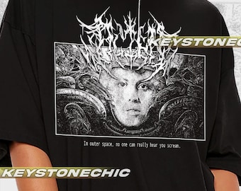 Puede incluir: Camiseta negra de gran tamaño con un estampado gráfico blanco de una cara rodeada de formas abstractas. El texto "In outer space, no one can really hear you scream." está impreso debajo del gráfico.