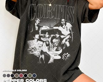 Puede incluir: Una camiseta de manga corta gris carbón con un gran estampado gráfico blanco de un grupo de personas y el texto CORTIS en una fuente serif negrita. La camiseta tiene un aspecto desgastado y un cuello redondo.