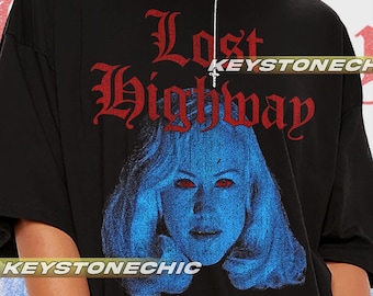 Puede incluir: Camiseta negra de gran tamaño con un estampado gráfico rojo y blanco de la cara de una mujer con el texto "Lost Highway" y "...Do you own a video camera?"