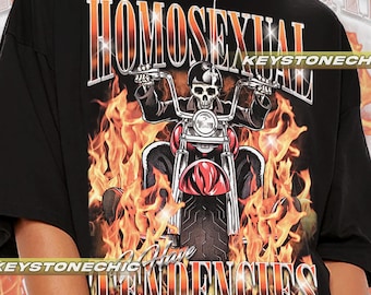 Puede incluir: Camiseta negra con un estampado gráfico de un esqueleto montando una motocicleta a través de llamas. El texto "HOMOSEXUAL HAVE TENDENCIES" está impreso en la camiseta.
