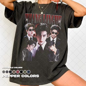 May include: Dark gray t-shirt featuring a graphic of five men in suits and sunglasses. The text "ZHANG LINGHE" is printed in red across the top. Below the graphic are the words "AVAILABLE COLORS" and "PEPPER COLORS".