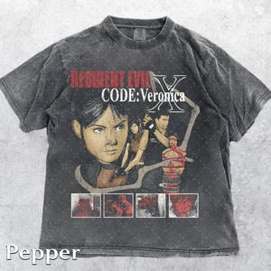 Könnte beinhalten: Dunkelgraues T-Shirt mit einer Grafik aus dem Videospiel Resident Evil Code: Veronica. Das Design zeigt ein Porträt einer Frau und anderer Charaktere. Der Text "RESIDENT EVIL X CODE: Veronica" ist oben aufgedruckt.