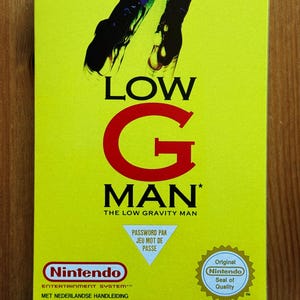 Puede incluir: Una caja de juego amarilla de Nintendo Entertainment System para "Low G Man". La caja presenta el título del juego en letras grandes rojas y negras, con el logotipo de Nintendo y "Original Nintendo Seal of Quality".