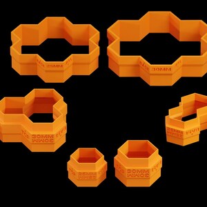 Puede incluir: Conjunto de nueve cortadores de galletas de plástico naranja con forma de panal. Los cortadores son de varios tamaños y tienen las palabras "Cookie Press" impresas.
