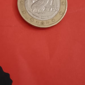 Può includere: Una moneta dorata con un centro argentato che presenta un gufo e il testo "1 EURO".