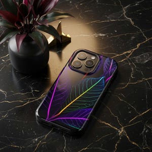 May include: A smartphone case featuring a dark background with a vibrant, glowing neon leaf pattern in shades of purple, blue, and yellow. The case has a precise cutout for the triple-lens camera system, showcasing a sleek and modern design.