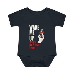 Puede incluir: Body de bebé azul marino con el texto "WAKE ME UP WHEN NAP TIME ENDS" en blanco y rojo. Un dibujo de una mano blanca sostiene un chupete rojo y blanco. Un divertido body para bebé.
