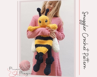 May include: A crocheted bee snuggle toy with black and yellow stripes, white wings, and black legs. The bee is being held by a child wearing a pink shirt. The text "Smuggler Crochet Pattern" is visible on the right side of the image.