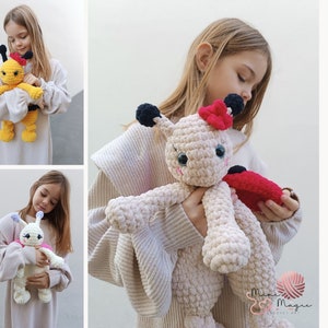 Pode incluir: Três brinquedos de pelúcia de crochê para aconchegar. Uma abelha amarela e preta, um caracol rosa e branco e uma joaninha creme com asas vermelhas. Os brinquedos estão sendo segurados por crianças.