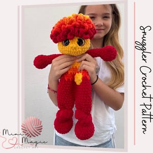 Puede incluir: Muñeca de ganchillo hecha a mano en rojo, amarillo y naranja. La muñeca tiene una cabeza grande y texturizada, ojos grandes y brazos y piernas extendidos. La muñeca está siendo sostenida por una persona. El texto "Snuggler Crochet Pattern" es visible.
