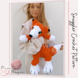 Könnte beinhalten: Ein gehäkeltes Fuchs-Plüschtier mit orangefarbenem und weißem Fell, das ein kleines grünes Herz hält. Der Fuchs wird von einer jungen Person gehalten, die einen weißen Pullover trägt. Das Bild enthält den Text "Smuggler Crochet Pattern".