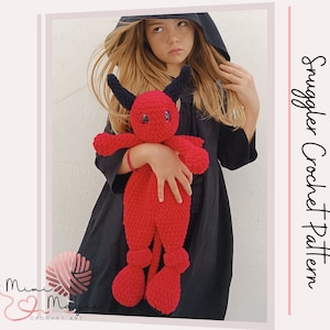 May include: A red crochet devil doll with black horns and blue eyes. The doll is held by a person wearing a dark hooded garment. The text "Snuggler Crochet Pattern" is visible on the right side of the image.