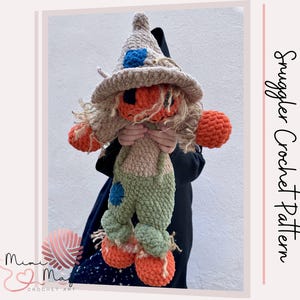May include: A plush scarecrow doll made of soft yarn, wearing a tan pointed hat with a blue patch, orange hands and feet, and green overalls with a blue patch. The doll has light brown yarn hair and text reading Snuggler Crochet Pattern.
