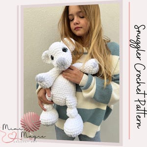 Pode incluir: Um animal de pelúcia branco de crochê que se assemelha a um urso polar, sendo segurado por uma pessoa jovem que veste um suéter listrado azul e branco. O texto "Smuggler Crochet Pattern" é visível no lado direito da imagem.
