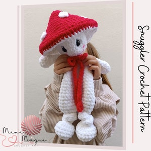 May include: A white crocheted mushroom amigurumi toy with a red crocheted hat. The toy has a red ribbon around its neck. The toy is being held by a person wearing a beige sweater.