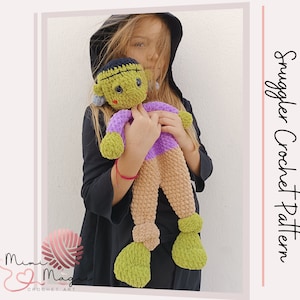 May include: A crocheted Frankenstein doll with green skin, purple shirt, and brown pants. The doll is being held by a person wearing a black hooded jacket.