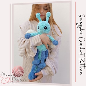 Puede incluir: Un juguete de peluche de insecto azul y verde tejido a crochet con grandes ojos negros. El juguete lo sostiene un niño que lleva un suéter de color crema.