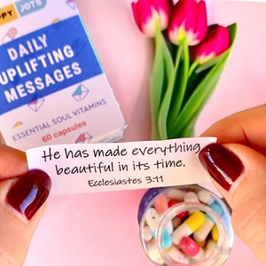 May include: A white card with the text "He has made everything beautiful in its time. Ecclesiastes 3:11" is held in a hand with red nail polish. The card is part of a set of daily uplifting messages.