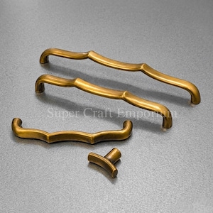 May include: A set of four antique brass cabinet hardware pieces. The set includes two long pulls, one shorter pull, and a small knob. The hardware has a curved, ornate design and a warm, golden finish.