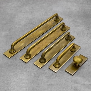 Könnte beinhalten: Eine Sammlung antiker Türgriffe und Knöpfe aus Messing in verschiedenen Größen. Die Hardware hat eine warme, gealterte Oberfläche und ein klassisches, gebogenes Griffdesign. Das Set umfasst lange Stangengriffe und einen runden Knopf.