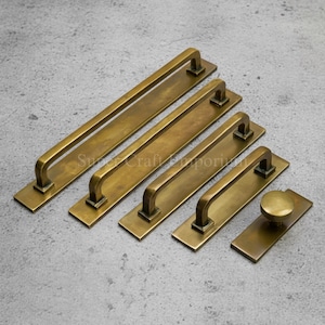 May include: A selection of antique brass door and drawer pulls in various sizes. The hardware features rectangular backplates and curved handles, with a matching round knob. The finish is a warm, aged brass.