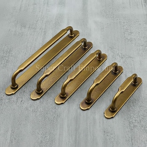 Peut inclure: Ensemble de poignées de meubles en laiton antique de différentes tailles. Chaque poignée présente une plaque arrière rectangulaire et une poignée incurvée. Le laiton a une finition vieillie, suggérant un aspect ancien. Idéal pour la restauration de meubles.