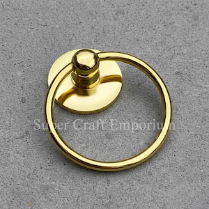 Könnte beinhalten: Ein goldfarbener Schrankgriff mit rundem Griff und runder Basis. Der Griff hat eine glänzende Oberfläche und der Text "Super Craft Emporium" ist auf der Basis sichtbar.