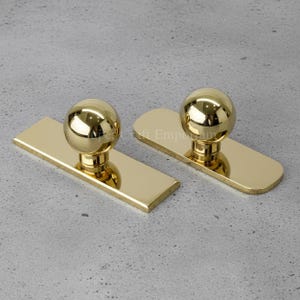 May include: Two polished gold door pulls. Each pull has a spherical knob on a rectangular base with rounded edges. The reflective surface gives a bright, luxurious look. Hardware for doors.
